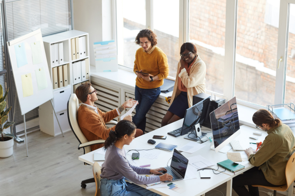 Five office workers collaborating around a table while seamlessly accessing accounts on different devices.