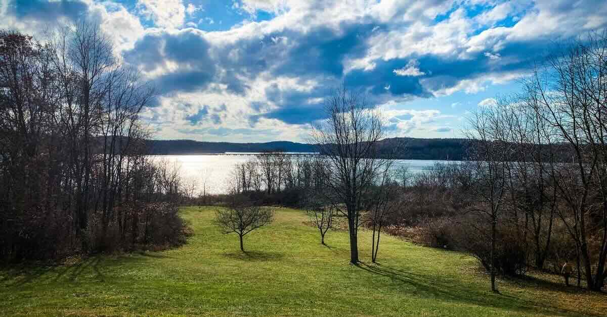 A well-mown disc golf fairway lined by trees with a view of a lake in the distance