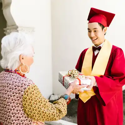 Man in red graduation gown gives gift to grandmother.