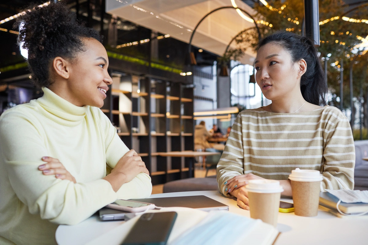 Two women in a coffee shop having a business meeting with notebooks, phones, and computers