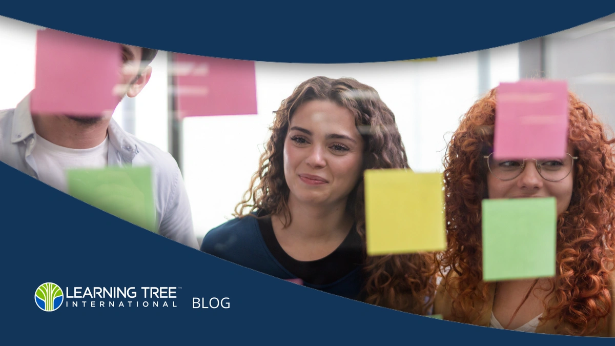 Three young businesspeople reading sticky notes on a glass wall, sharing ideas during a creative meeting.
