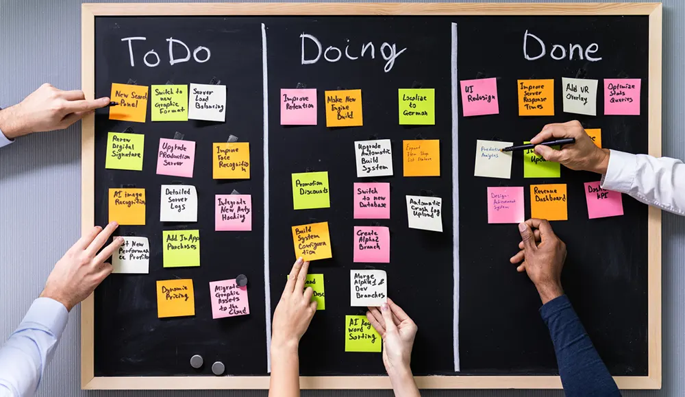 black board with hands placing multiple sticky notes under to do titles