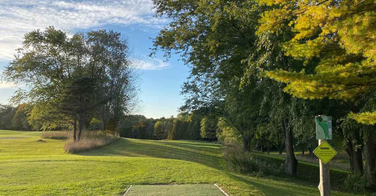 A turf tee pad leads to a well-mown fairway lined with mature trees