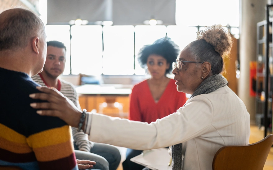 Senior woman comforting a mature man in group therapy at a coworking