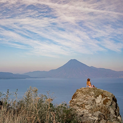 a woman sitting on top of a rock next to a body of water