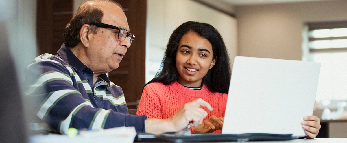 A teenager helps an older man set up a secure home network on his laptop.