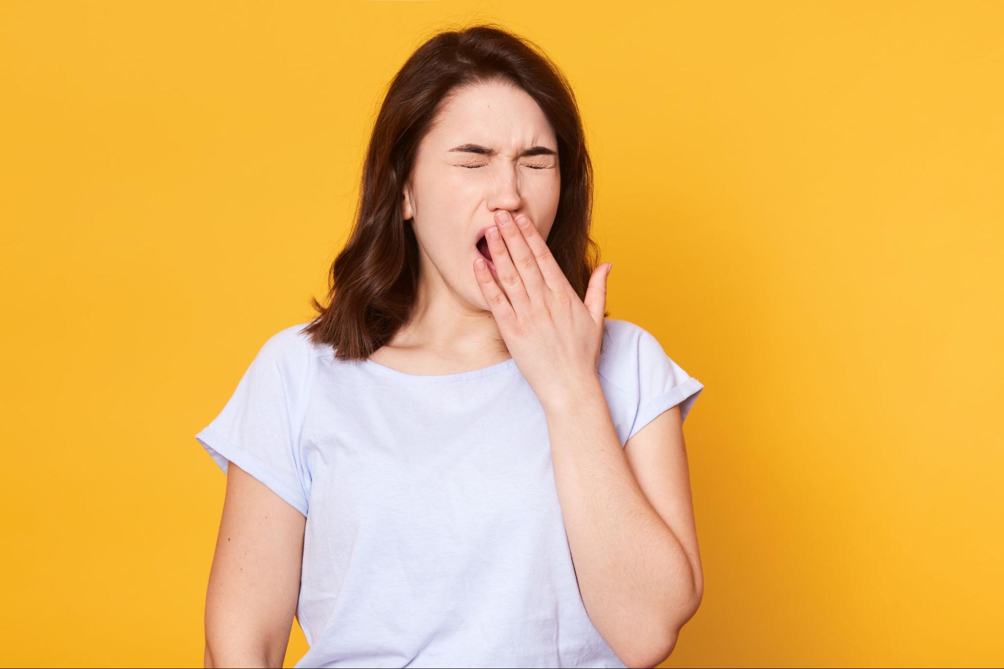 how to get water out of your ear: Yawning woman against a yellow background