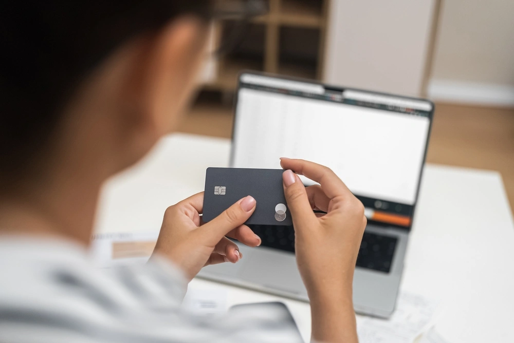 Woman holding a credit card with the image of a laptop in the background